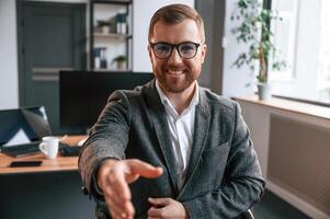 Giving the hand, greetings gesture. Businessman in suit is in the office with computer photo