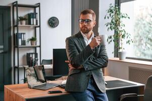 Leaning on, the table. Businessman in suit is in the office with computer photo
