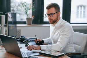 Side view. Man in formal clothes is, working in the modern office. Using computer photo