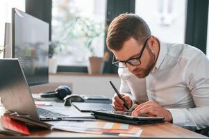 Using ,tablet. Man in formal clothes is working in the modern office photo