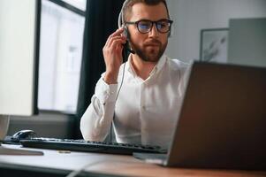 In ,headphones. Man in formal clothes is working in the modern office. Using computer photo