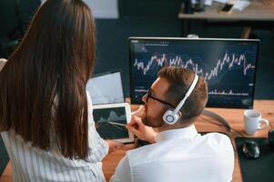 Two office, workers are analyzing graphs that on the computer screen photo