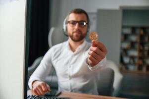 Holding, bitcoin in the hand. Man in formal clothes is working in the modern office. Using computer photo