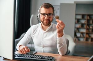 Holding ,bitcoin ,in the hand. Man in formal clothes is working in the modern office. Using computer photo