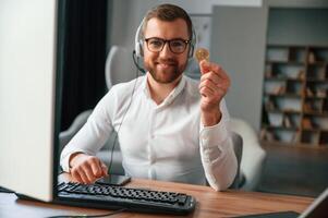 Holding, bitcoin ,in the hand. Man in formal clothes is working in the modern office. Using computer photo