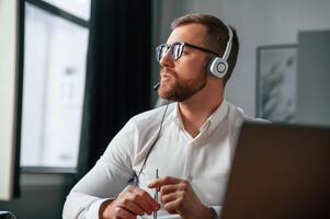 In ,headphones.. Man in formal clothes is working in the modern office. Using computer photo
