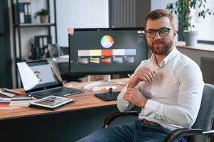 Graphic designer is sitting. Man in formal clothes is working in the modern office. Using computer photo