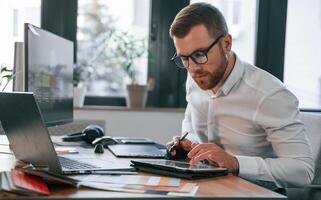 Using tablet. Man in formal clothes is working in the modern office photo