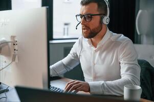 In the ,call center.. Wearing headphones. Office worker in formal clothes is sitting by computer and working photo
