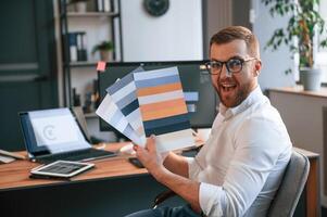Designer, is ,choosing different colors for project. Man in formal clothes is working in the modern office. Using computer photo