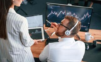 Two office workers are analyzing graphs that on the computer screen photo
