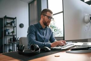 Typing on, the keyboard.. Man in formal clothes is working in the modern office. Using computer photo