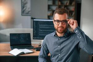 Software developer is sitting and posing.. Man in formal clothes is working in the modern office. Using computer photo