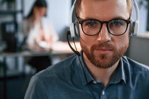 Portrait of man. Woman is on background. Two employees are working together in the modern office photo