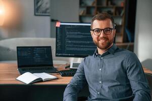 Software developer is sitting and posing. Man in formal clothes is working in the modern office. Using computer photo