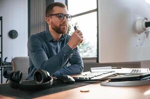 Smoking electric cigarette. Man in, formal, clothes is working in the modern office. Using computer photo