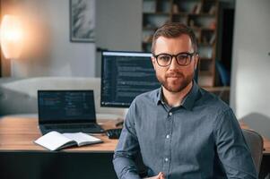 Software ,developer, is sitting and posing. Man in formal clothes is working in the modern office. Using computer photo