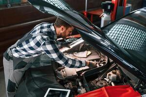 Under the hood.. Holding lighting equipment and fixing the issues of the car. Man in uniform is working in the auto salon photo
