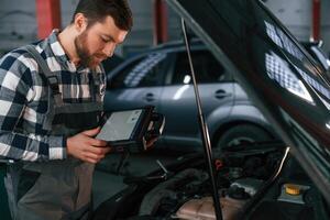 With, tablet in ,hands. Man in uniform is working in the auto salon photo