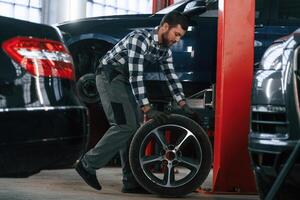 Side view.. Moving, the tire for the car. Man in uniform is working in the auto salon photo
