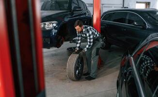 Front, left ,wheel is changing. Man in uniform is working in the auto salon photo