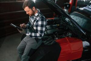 With tablet in hands. Man in uniform is working in the auto salon photo