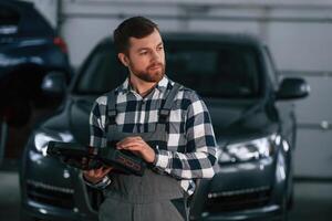 Holding, tablet. Man in, uniform is working in the auto salon photo
