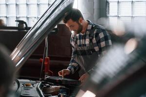 Hood ,of, the car is opened. Using tablet. Man in uniform is working in the auto salon photo