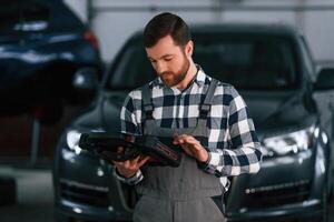 Holding tablet. Man, in uniform is working in the auto salon photo