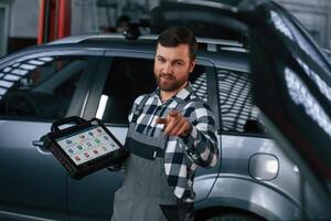 Showing gesture,and smiling. Holding tablet. Man in uniform is working in the auto salon photo