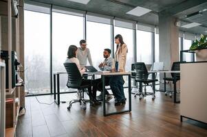 Against big windows, by the table. Four people are working in the office together photo