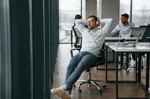 Relaxed,, on the chair,, in headphones. Men and woman are working in the office together photo
