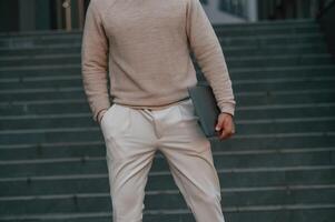 Close, up view, of man that is standing against the stairs outdoors and holding laptop photo