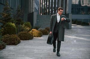 Checking the time. Handsome man in formal clothes is outdoor near the business building photo