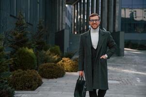 Smiling, feeling ,good. Handsome man in formal clothes is outdoor near the business building photo