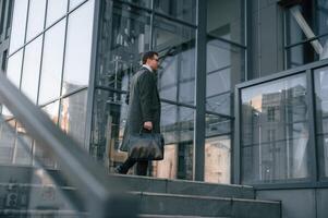 Holding the, bag. Handsome, man in formal clothes is outdoor near the business building photo