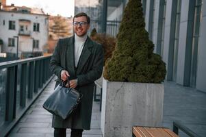Holding the, bag. Handsome man in formal clothes ,is outdoor near the business building photo