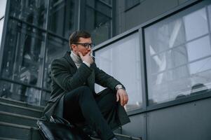 Sitting on the, stairs and smoking. Handsome, man in formal clothes is outdoor near the business building photo