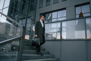 Holding, the, bag. Handsome, man in formal clothes is outdoor near the business building photo