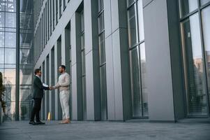 With notepat and ,documents., Businessman in formal ,clothes is with black man outdoors in the city photo