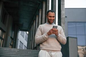 Enjoying social, media by using ,smartphone. Handsome black man is outdoors near the business building photo