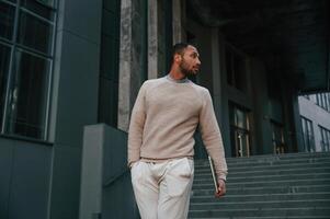 Front view., Standing with,aptop in hands. Handsome black man is outdoors near the business building photo