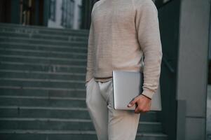 Close up view of man that is standing against the stairs outdoors and holding laptop photo