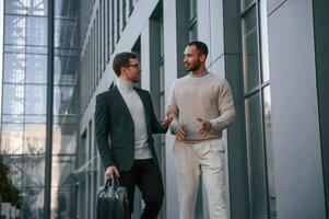 Walking together. Businessman, in formal clothes, is with black man outdoors in the city photo