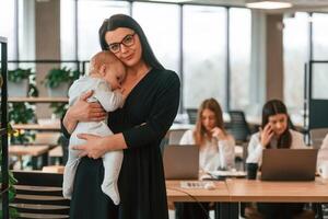Infant, baby is in the office where group of people are working together photo