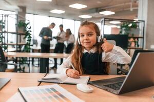 Laptop is on the table., Little girl is in the office where people working together photo