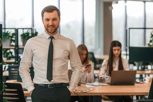 Man in tie is standing in front ,of his colleagues. Business people in formal clothes are working in the office together photo