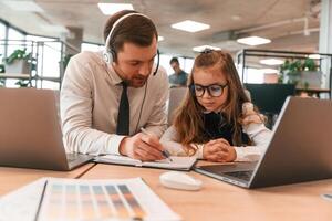 Man is helping,, teaching. Little girl is in the office where people working together photo