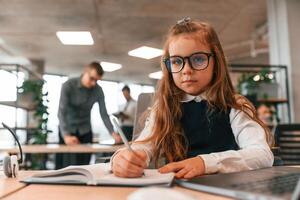 Laptop is on the table. Little girl is in the office where, people working together photo