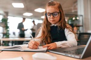 Laptop is on the table. Little girl is in, the office ,where people working together photo